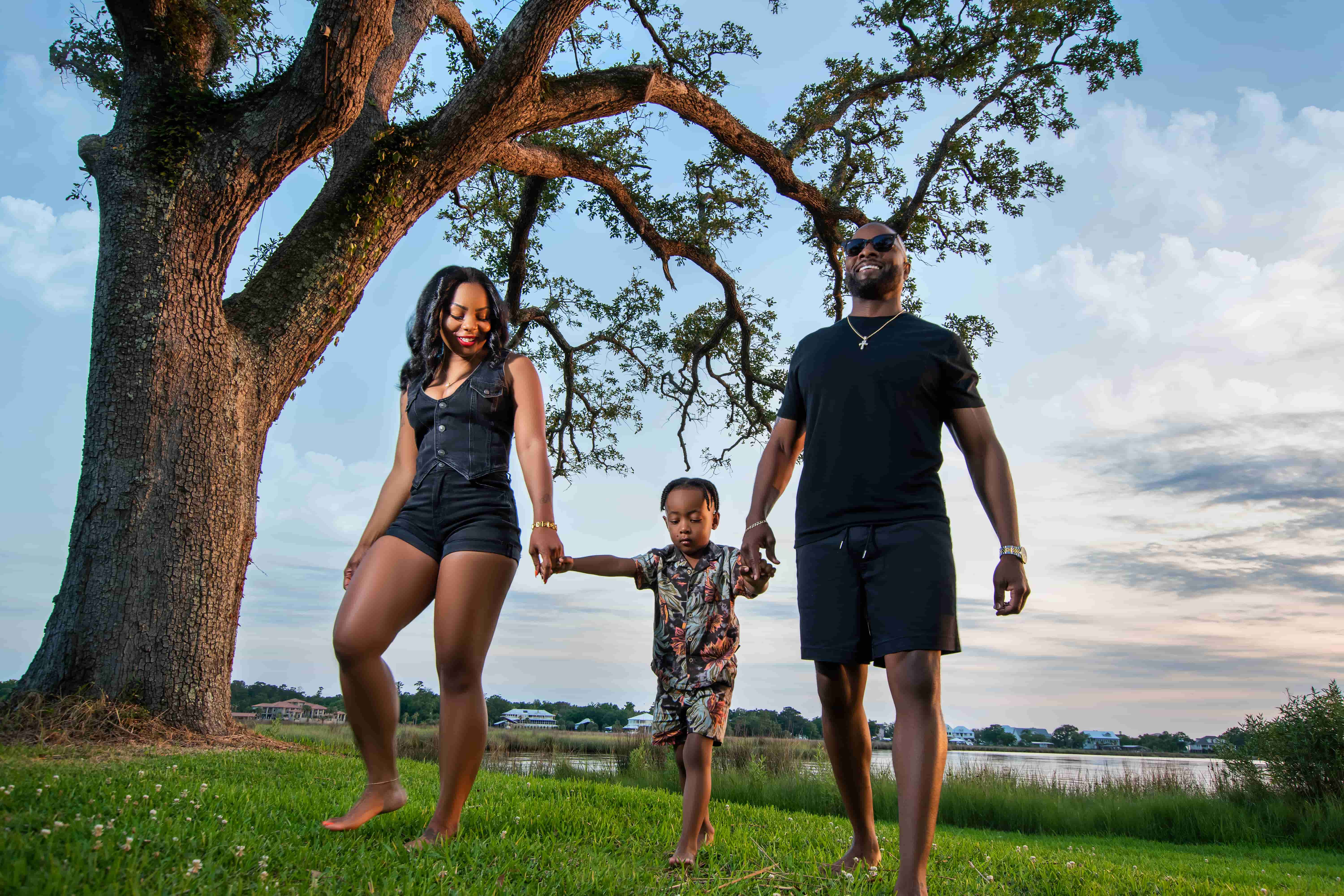 Family of three walking barefoot hand in hand under a live oak by the bayou in Biloxi, MS