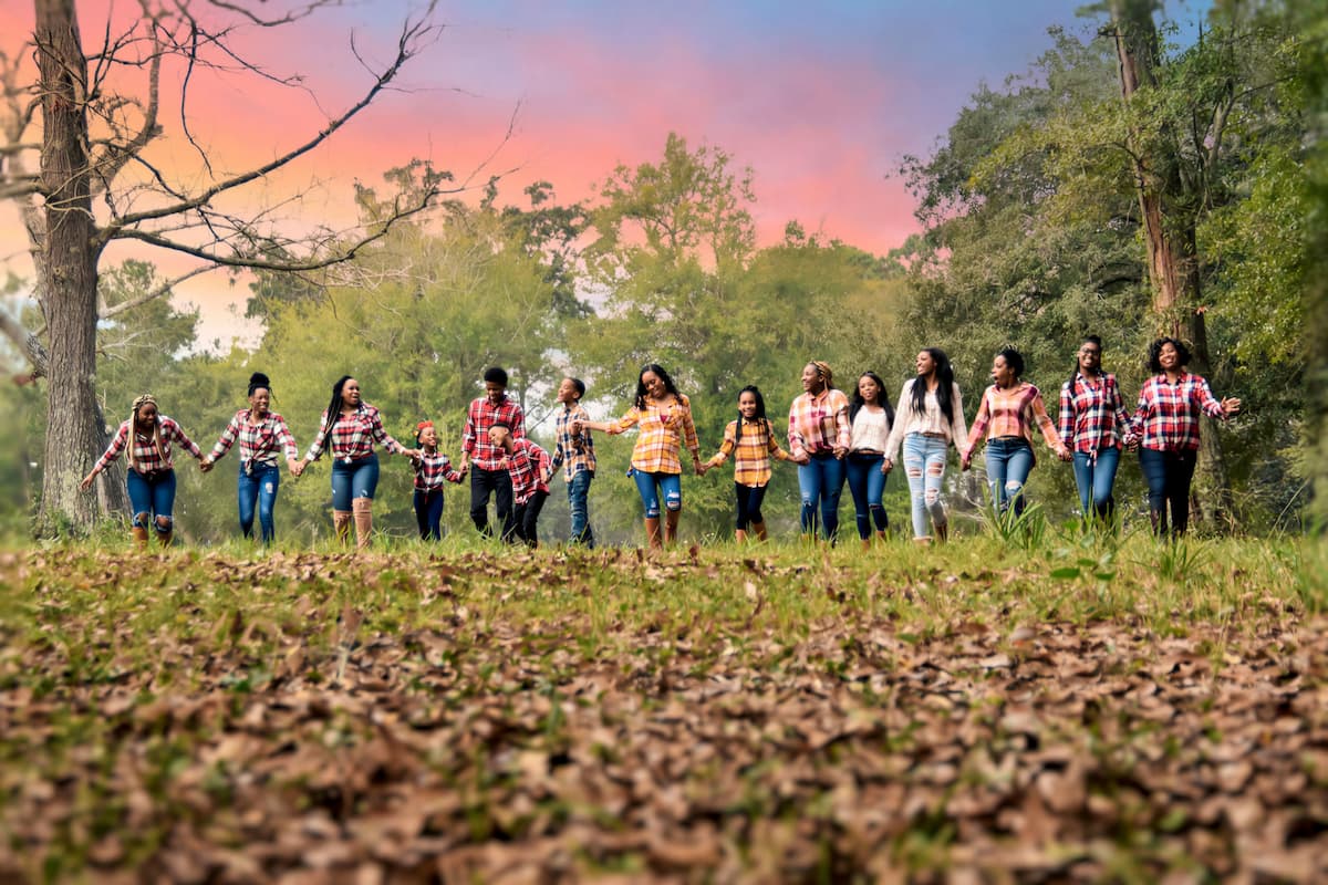 Extended family in matching plaid shirts walking hand in hand through a wooded field at sunset, photographed by DP Photography in Biloxi, MS.