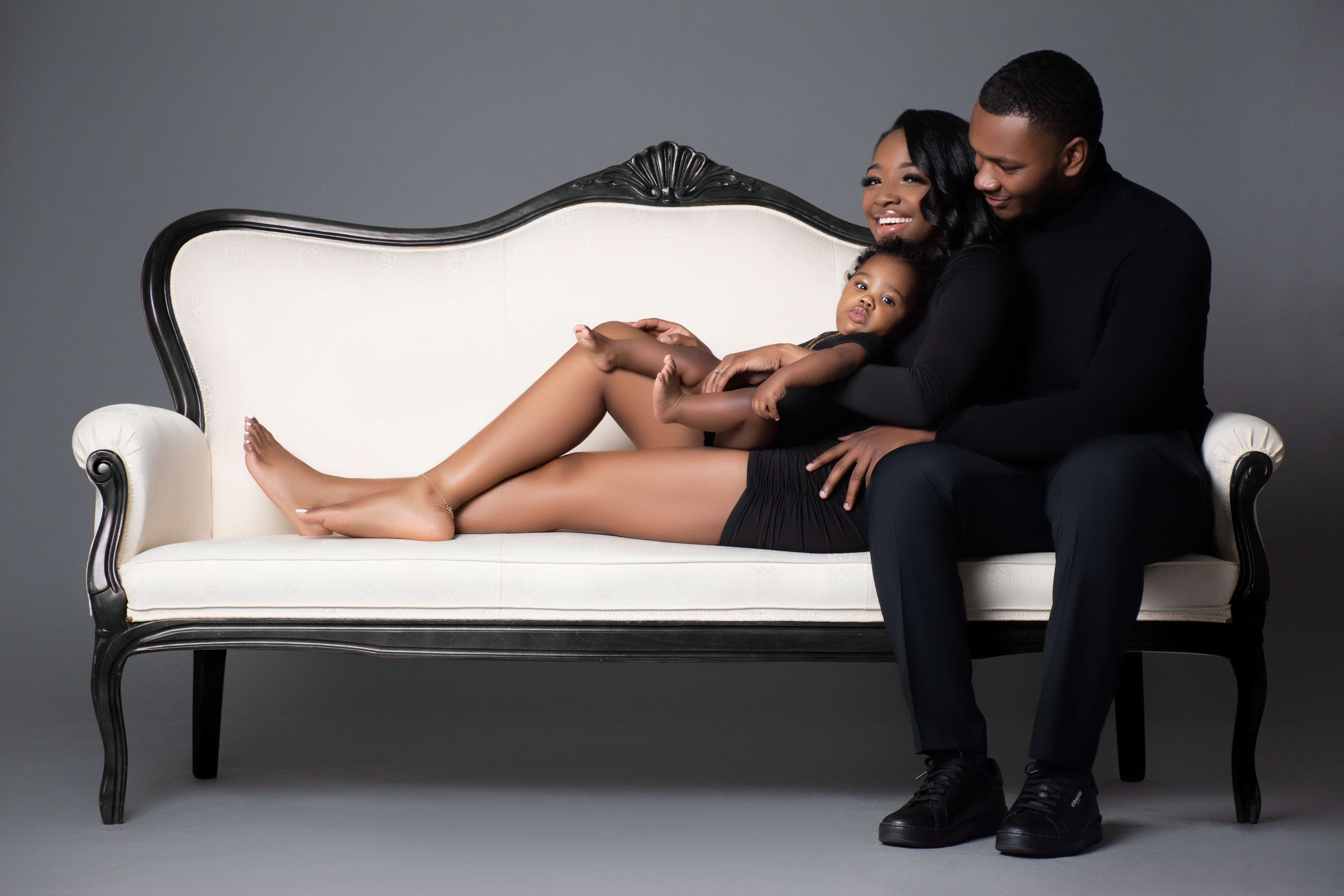 Laughing young family with their baby relaxing on an ivory Victorian settee at the DP Photography studio in Biloxi, MS.