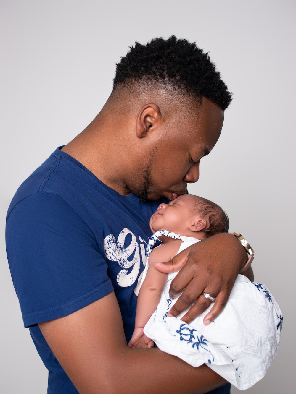 Father gently kissing his sleeping newborn daughter's forehead at the DP Photography studio in Biloxi, MS.